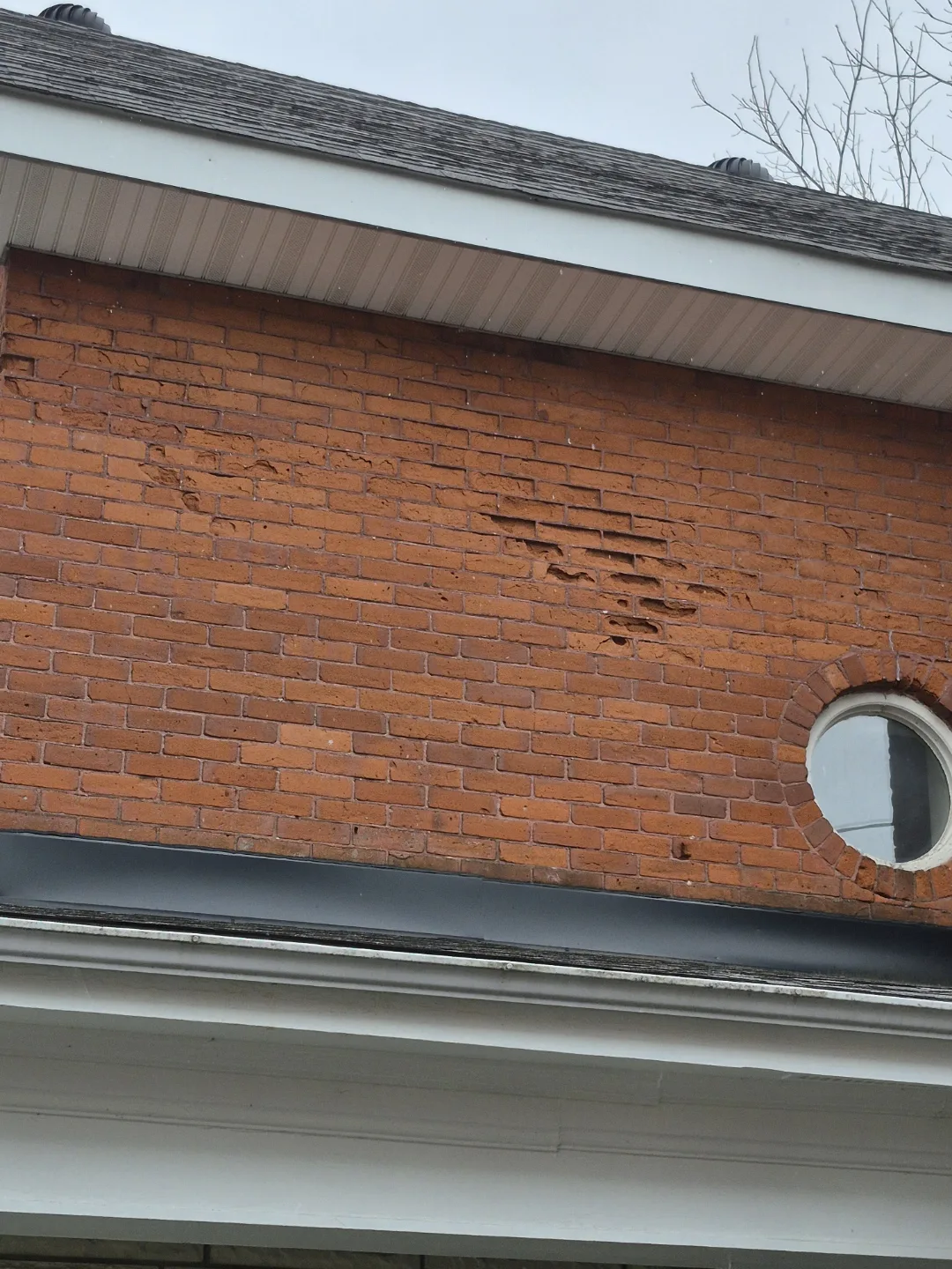 Spalling brick damage on the upper wall of a century home before repair
